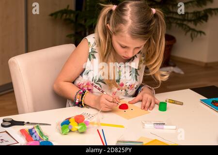 adorable fille avec des papiers colorés, des ciseaux, de la colle, des pailles, des crayons, des rubans, de la dentelle sur la table makint cartes de noël uniques Banque D'Images