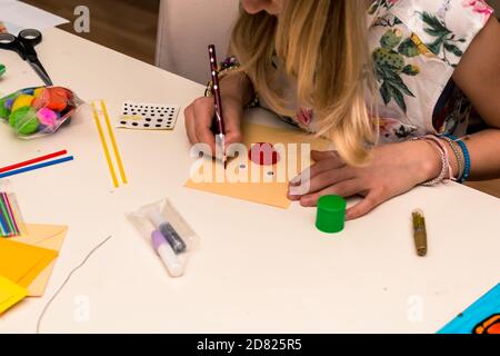 adorable fille avec des papiers colorés, des ciseaux, de la colle, des pailles, des crayons, des rubans, de la dentelle sur la table makint cartes de noël uniques Banque D'Images