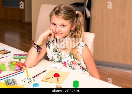 adorable fille avec des papiers colorés, des ciseaux, de la colle, des pailles, des crayons, des rubans, de la dentelle sur la table makint cartes de noël uniques Banque D'Images