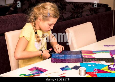 adorable fille avec des papiers colorés, des ciseaux, de la colle, des pailles, des crayons, des rubans, de la dentelle sur la table makint cartes de noël uniques Banque D'Images