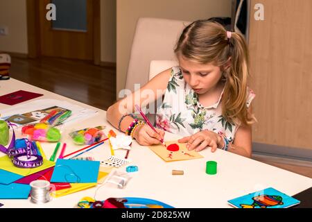 adorable fille avec des papiers colorés, des ciseaux, de la colle, des pailles, des crayons, des rubans, de la dentelle sur la table makint cartes de noël uniques Banque D'Images