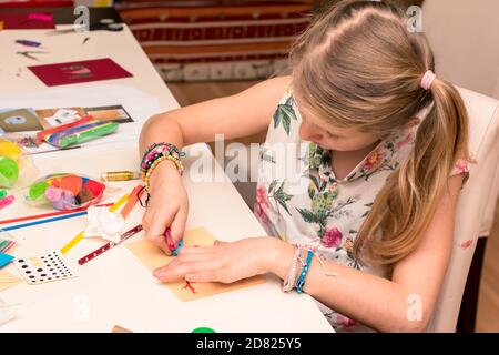 adorable fille avec des papiers colorés, des ciseaux, de la colle, des pailles, des crayons, des rubans, de la dentelle sur la table makint cartes de noël uniques Banque D'Images