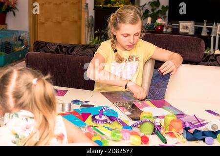 adorable fille avec des papiers colorés, des ciseaux, de la colle, des pailles, des crayons, des rubans, de la dentelle sur la table makint cartes de noël uniques Banque D'Images