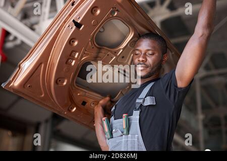 afro american auto mécanicien va changer partie séparée de l'automobile. tenir le métal lourd dans la main Banque D'Images