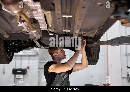 un mécanicien de sexe masculin travaille sur un véhicule dans un service de voiture, seul dans un atelier moderne et propre Banque D'Images