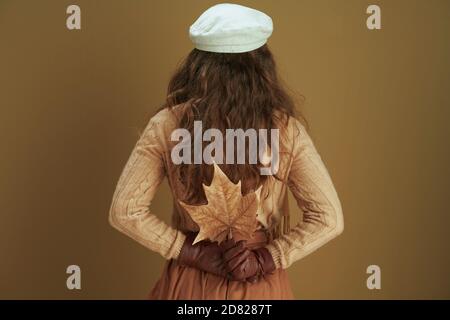 Bonjour automne. Vue de derrière une femme en foulard avec des feuilles d'érable jaune d'automne isolées sur fond de bronze. Banque D'Images