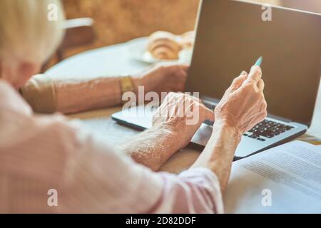 Photo rognée d'une femme âgée tenant un stylo tout en pointant sur l'écran d'un ordinateur portable. Copier l'espace. Concept de famille et de ménage Banque D'Images