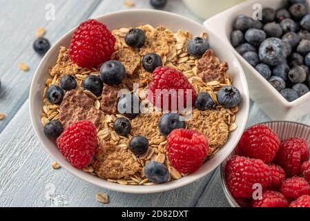 Granola aux bleuets et framboises dans un bol blanc sur un bureau blanc foncé. Banque D'Images