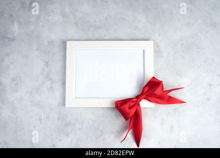 Cadre blanc avec noeud rouge sur béton gris. Banque D'Images