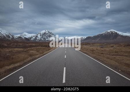 La route menant aux montagnes enneigées à travers la vallée. Highlands écossais de Glen COE. Écosse, Royaume-Uni Banque D'Images