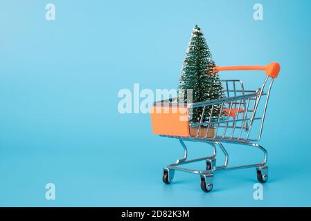 Préparation du concept de Noël. Gros plan photo pleine grandeur du petit jouet vert dans l'arbre de neige se tenant à l'intérieur dans le chariot isolé sur le dos bleu Banque D'Images