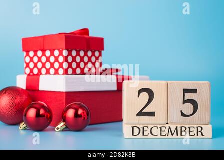 Concept Joyeux Noël. Gros plan photo de bloc de calendrier en bois montrant le 25 décembre et pile de rouge présente des boules isolées sur fond bleu Banque D'Images