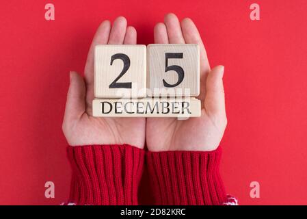 Haut au-dessus de la tête gros plan première personne voir la photo de Les mains des adolescentes tiennent le calendrier en bois avec la date de Noël isolée sur fond rouge Banque D'Images