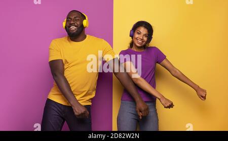 Couple avec casque écouter de la musique et danser avec énergie sur fond violet et jaune Banque D'Images