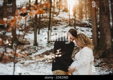 Couple avec les mains sur le ventre enceinte à l'extérieur en hiver une journée ensoleillée Banque D'Images