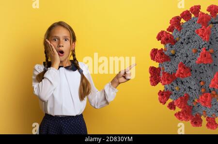 Le jeune étudiant est avec une expression choquée et indique la bactérie Covid-19. Arrière-plan jaune. Banque D'Images