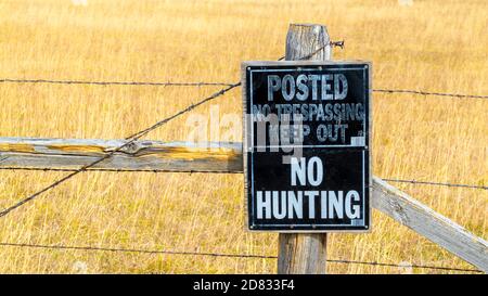 Un panneau No Hunting est affiché sur un fil barbelé en bois clôture dans un champ d'herbe sauvage dorée pendant la chasse saison avec espace de copie Banque D'Images