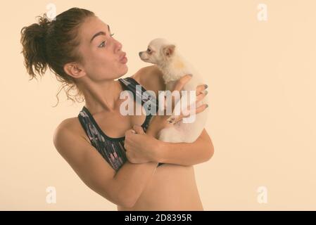 Portrait of teenage girl holding tout en embrassant mignon chien prêt pour le sport et l'exercice contre fond blanc Banque D'Images