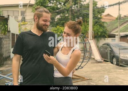 Happy young couple smiling while using mobile phone ensemble dans l'ancienne aire de jeux Banque D'Images