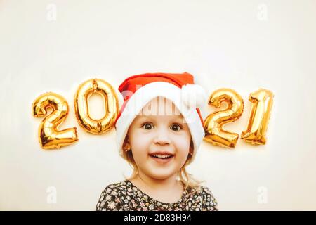 Une petite fille de Santa Cap sourit sur le fond de numéros d'or 2021 Banque D'Images