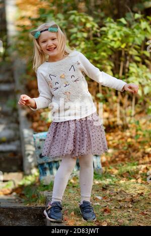 Adorable happent r blonde petite fille portant des oreilles de chat, chandail de chat et jupe fantaisie riant à l'extérieur lors d'une belle journée d'automne. Style chat pour les vacances Banque D'Images