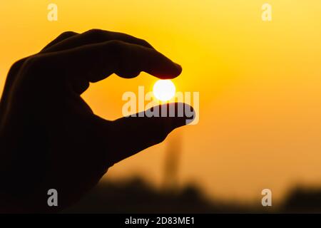Silhouette de doigt tenant le soleil orange sur un magnifique fond de coucher de soleil. Banque D'Images