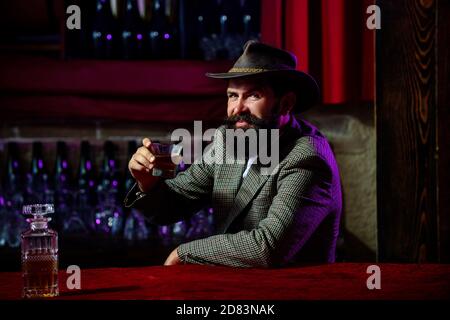 Homme avec la barbe tient le brandy de verre. Un homme barbu boit du cognac. Homme tenant un verre de whisky. Chuchotement. Portrait d'un homme avec une barbe épaisse. Macho Banque D'Images