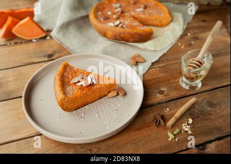 morceau de tarte juteuse à la citrouille avec amandes et miel, tarte entière sur une serviette en toile rugueuse sur table en bois avec morceaux de citrouille, miel, cannelle et anis. Banque D'Images