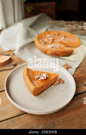 tarte à la citrouille aux amandes et au miel, tarte entière sur une serviette en toile rugueuse sur une table en bois avec des morceaux de citrouille, de miel, de cannelle et d'anis. confortable Banque D'Images