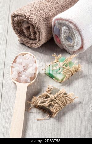 Wooden spoon with white sea salt and handmade soap for bathroom procedures with towels on the background. Spa products and accessories Banque D'Images