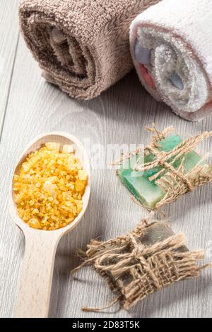 Wooden spoon with yellow sea salt and handmade soap for bathroom procedures with towels on the background. Spa products and accessories Banque D'Images