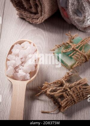 Wooden spoon with white sea salt and handmade soap for bathroom procedures with terry towels on the background. Spa products and accessories Banque D'Images