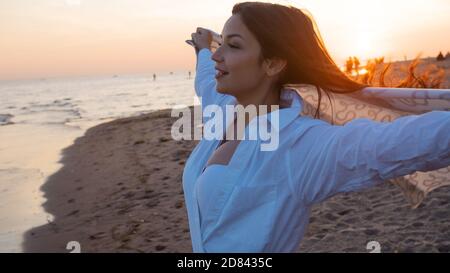 Jeune belle femme enveloppée dans une couverture chaude, chaude et confortable sur la plage. Courir sur la plage au coucher du soleil, se sentir libre et heureux. Banque D'Images