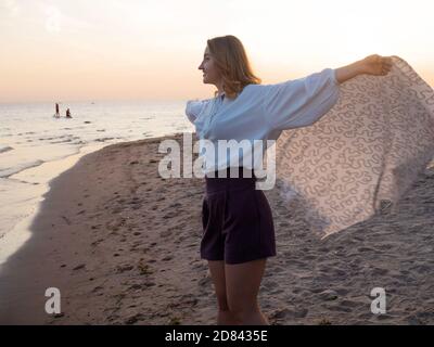 Jeune belle femme enveloppée dans une couverture chaude, chaude et confortable sur la plage. Courir sur la plage au coucher du soleil, se sentir libre et heureux. Banque D'Images