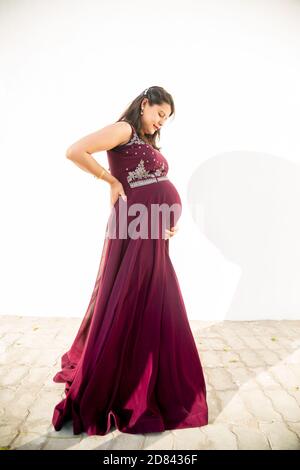 Jeune femme enceinte regardant le ventre debout sur fond blanc studio de tir, heureuse femme s'attendant à bébé, maternité et grossesse con Banque D'Images