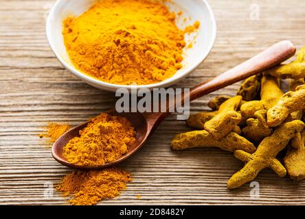 Poudre curcuma jaune et racines sèches sur fond de bois. Banque D'Images