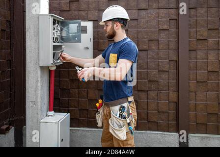 Électricien au travail, examine la connexion de câble dans la ligne électrique dans le fuselage d'un tableau de commutation industriel. Professionnel dans l'overal Banque D'Images