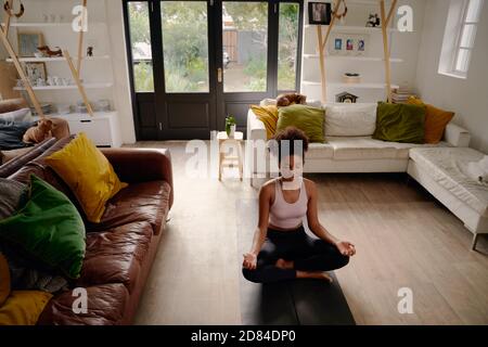 Jeune africaine jeune femme en position lotus pratiquant la méditation et exercice de respiration dans le salon à la maison Banque D'Images
