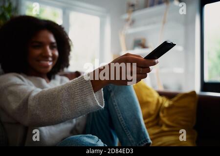 Femme changeant de chaîne de télévision à l'aide de la télécommande à la maison pendant le covid-19 Banque D'Images