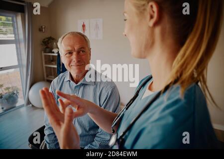 Souriant retraité homme patient à l'écoute de jeune femme médecin pendant expliquer le traitement de physiothérapie Banque D'Images