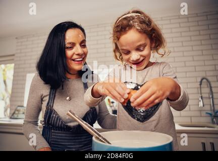 Une mère souriante aide sa fille à briser l'œuf pour préparer la pâte cuisine Banque D'Images