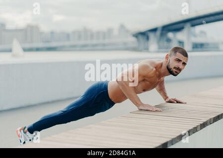 Plein plan de l'homme musclé sportif dans les vêtements de sport pousse vers le haut l'exercice a concentré l'expression sérieuse pose en extérieur. Auto-déterminé barbu Banque D'Images