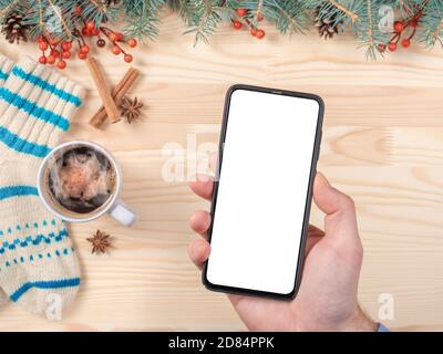 Image de maquette d'un homme tenant un téléphone portable noir avec écran vierge sur fond de noël. Smartphone à portée de main pour la saison de Noël Banque D'Images