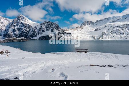 Un banc vide surplombant le lac de Luenersee avec les montagnes des Alpes en arrière-plan pendant la journée de neige à Brand, Bludenz, Vorarlberg, Autriche Banque D'Images