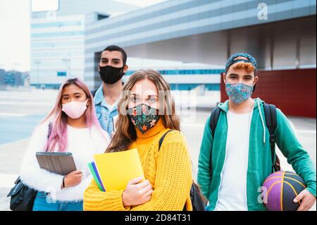 Amis multiraciaux sans souci portant un masque de protection pour passer du temps ensemble dans la ville en temps de coronavirus et souriant à la caméra Banque D'Images