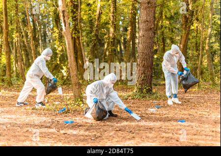 Les travailleurs en costume de protection avec des masques de visage, recueille des protections médicales sales pour le covid-19 dans un parc - concept d'écologie et de pleine conscience après le coronavi Banque D'Images