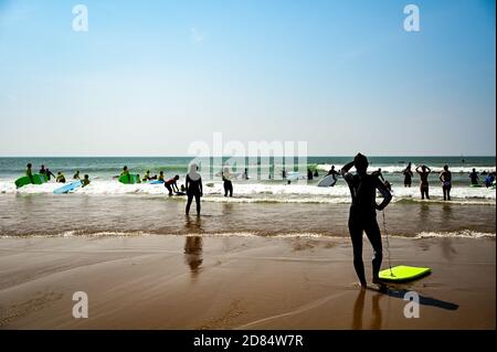 Les surfeurs jouent au bord de la plage sous le soleil d'été dans des combinaisons à Croyde Bay, Devon Banque D'Images