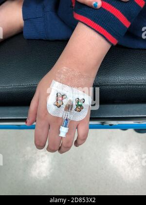 Une jeune fille asiatique avec une canule insérée dans sa main gauche à l'hôpital, afin d'administrer des liquides intraveineux. Banque D'Images