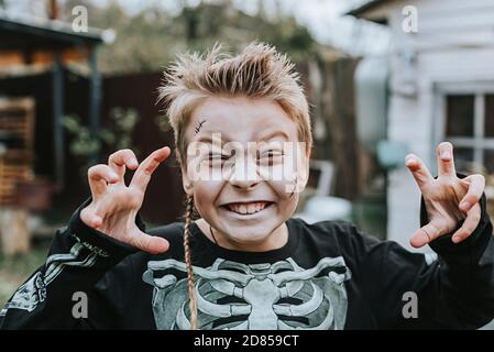 un garçon dans un costume de squelette avec un visage peint sur le porche d'une maison décorée pour célébrer un Fête d'Halloween Banque D'Images