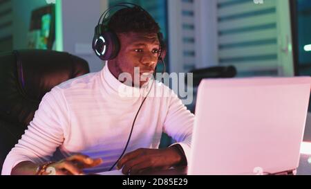 Jeune homme noir heureux avec casque lumineux utilisant un ordinateur portable. Concept de bureau à domicile et de travail à distance. Portrait du négociant boursier. Photo de haute qualité Banque D'Images